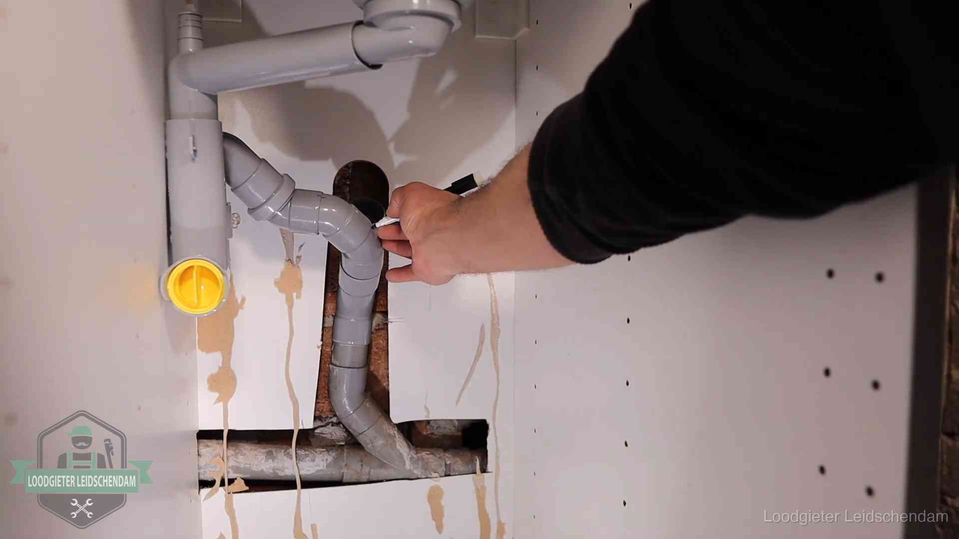 Loodgieter voor verhuurders en bedrijven in Leidschendam Loodgieter markeert een pvc-afvoerbuis onder een gootsteen in Leidschendam