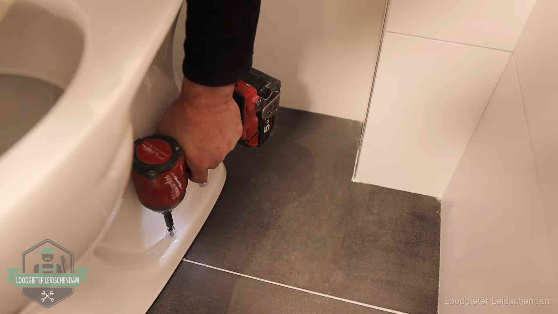 Kosten wc ontstoppen in Leidschendam Loodgieter zet de voet van een wc-pot vast op de tegelvloer in Leidschendam